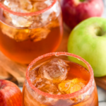 Pinterest graphic of fireball whiskey punch. Text says "The best fireball whiskey punch only uses 3 simple ingredients! shakedrinkrepeat.com" Image shows two glasses of fireball whiskey punch with ice, rimmed with red sugar. Apples and cinnamon sticks sitting beside.