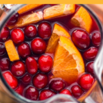 Pinterest graphic for friendsgiving sangria. Text says "Friendsgiving sangria so easy! shakedrinkrepeat.com" Image shows overhead of pitcher of friendsgiving sangria garnished with cranberries and orange slices/