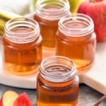 four shot glasses of washington apple shot recipe with apple slices sitting beside
