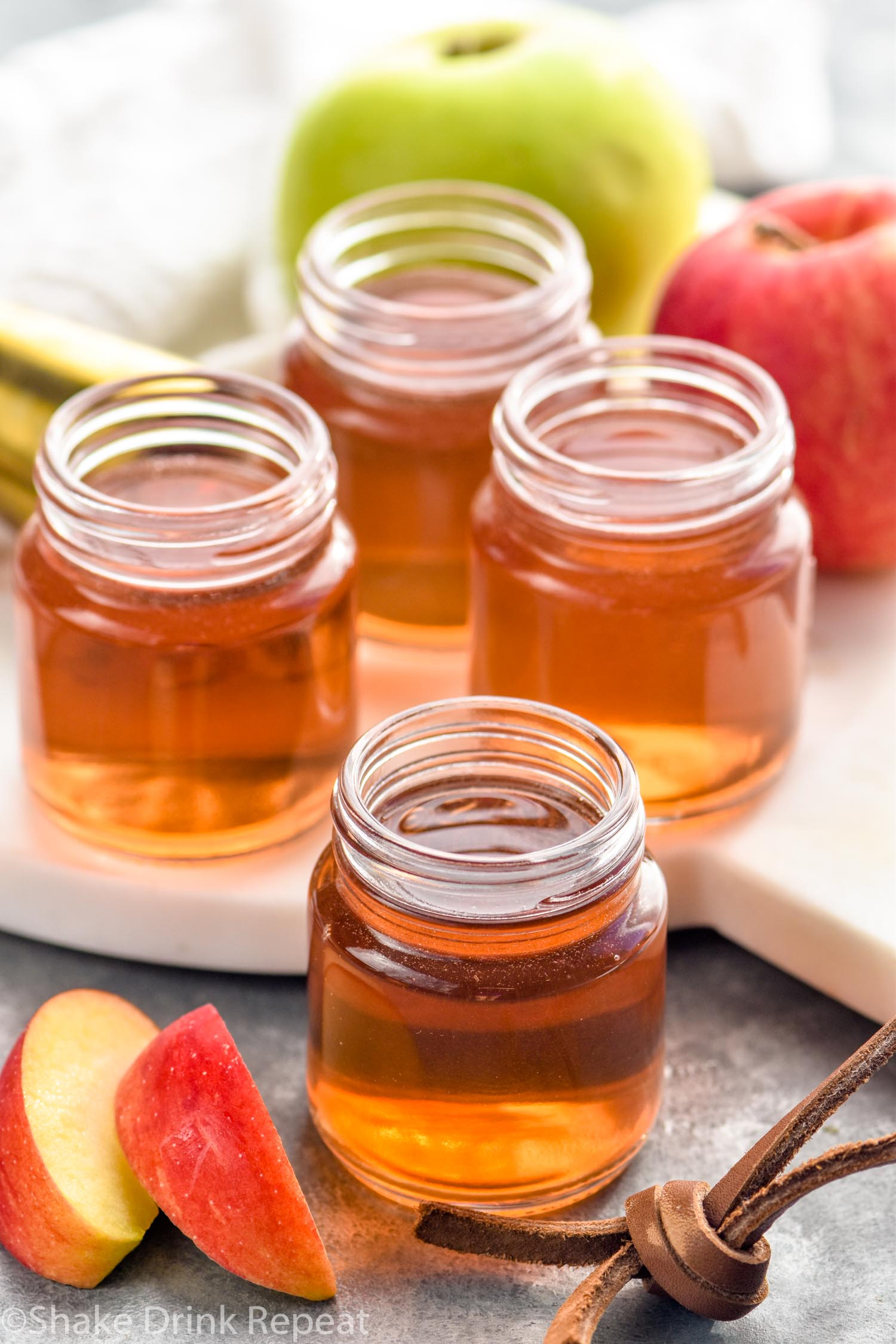 four shot glasses of washington apple shot recipe with apple slices sitting beside