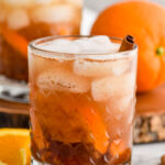 two glasses of fall spiced old fashioned cocktails with ice. Orange slices and cinnamon sticks sitting beside.