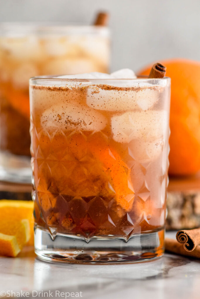 two glasses of fall spiced old fashioned cocktails with ice. Orange slices and cinnamon sticks sitting beside.