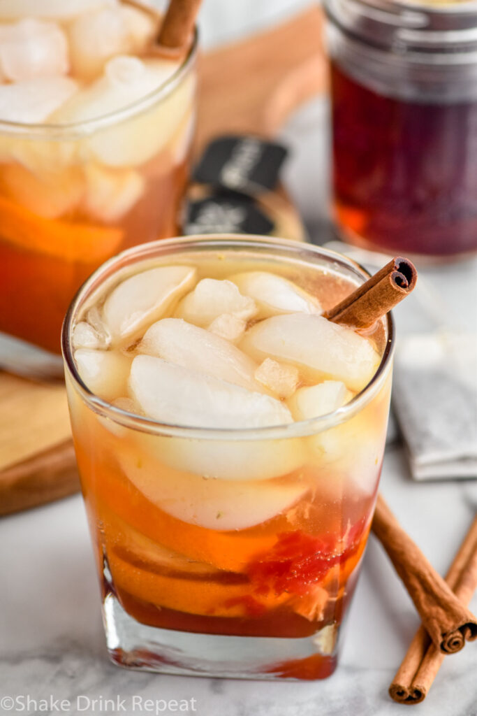 Photo of Chai Old Fashioned garnished with a cinnamon stick. jar of chai simple syrup is in the background.