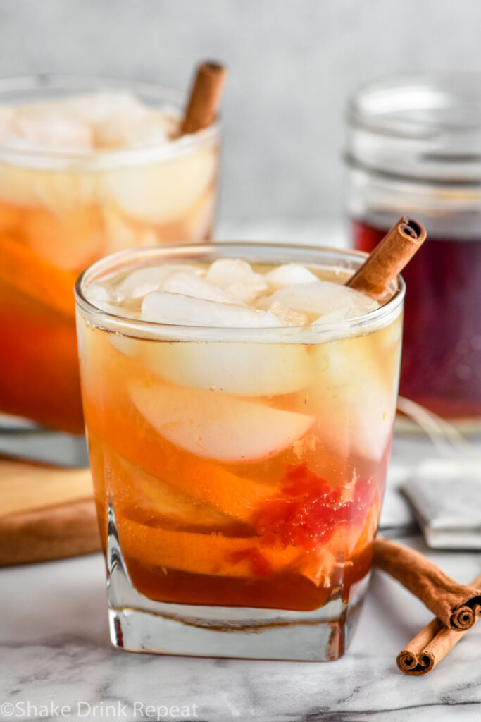 Photo of Chai Old Fashioned garnished with a cinnamon stick. jar of chai simple syrup is in the background.