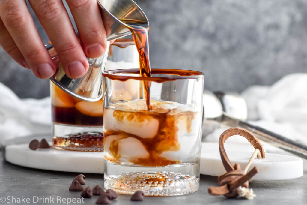 Photo of person's hand pouring chocolate liqueur into chocolate white russian recipe.