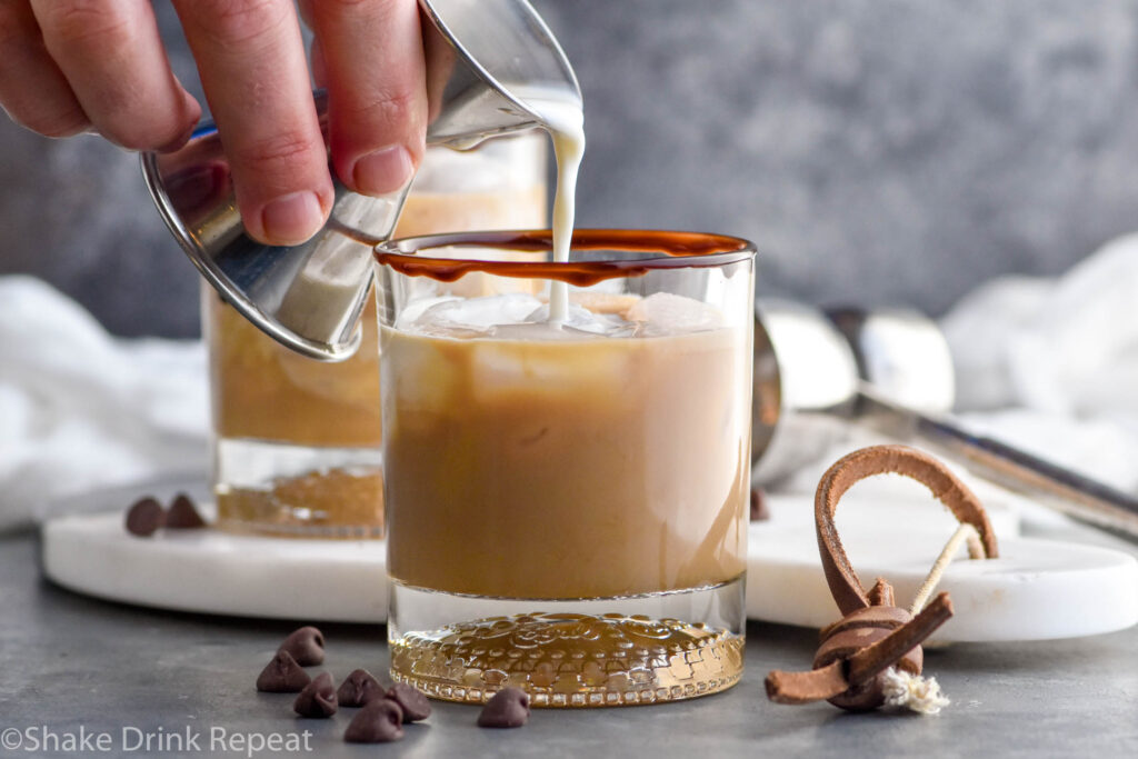Photo of person's hand pouring heavy cream into chocolate white russian cocktail.