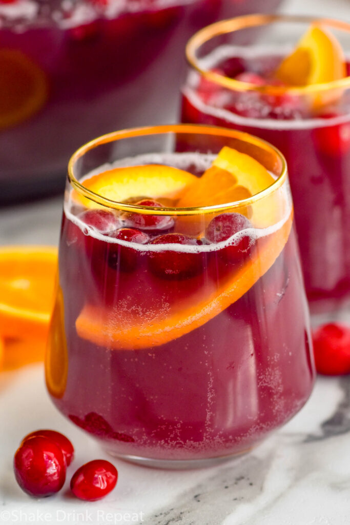 two glasses of Christmas punch garnished with orange slices and cranberries, cranberries laying beside glass.