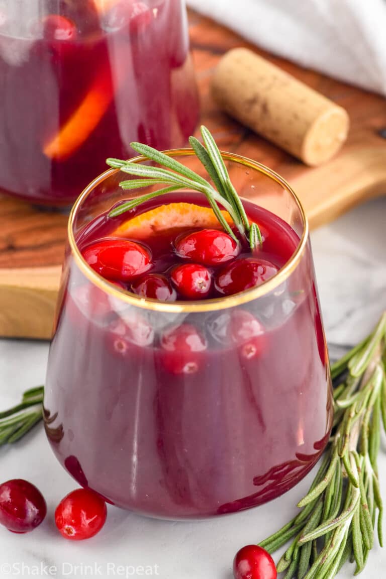 glass of cranberry orange sangria garnished with cranberries and a rosemary sprig with extra cranberries and rosemary sitting beisde