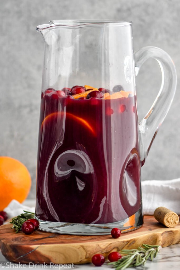 pitcher of friendsgiving sangria with cranberries, rosemary and orange sitting next to and in background