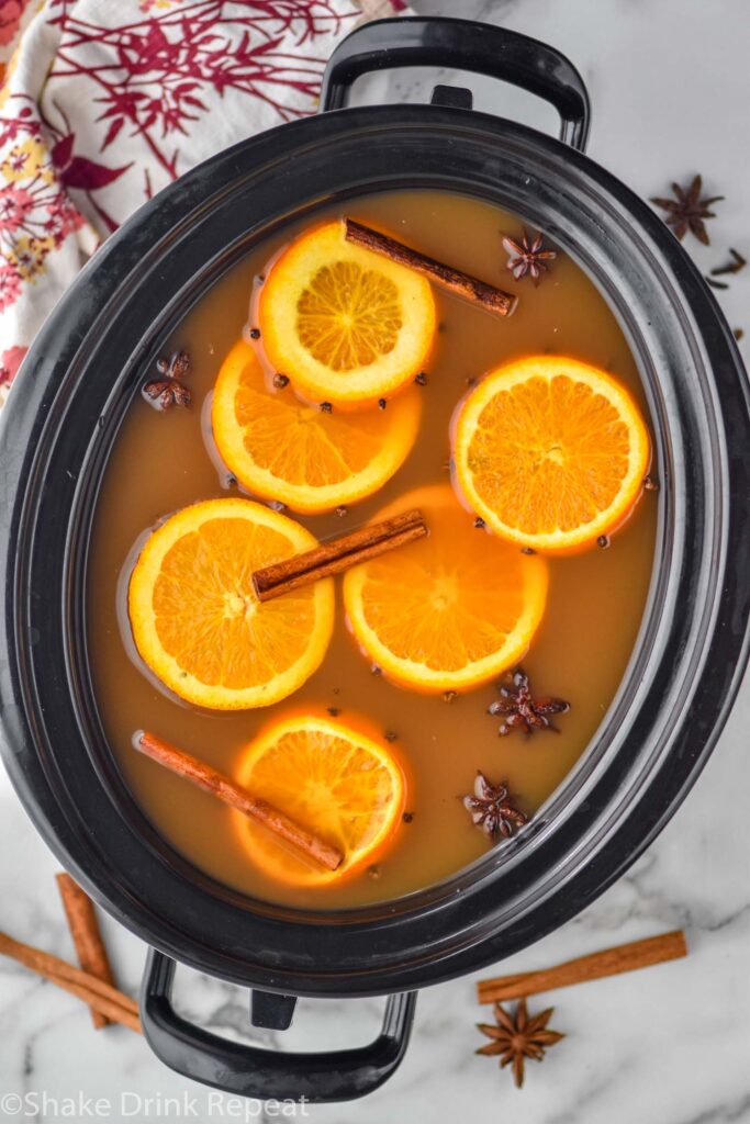 overhead of crockpot spiced apple cider with orange slices, cinnamon sticks, and star anise