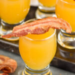 shot glass of breakfast shot recipe topped with bacon, glasses of breakfast shots sit in background