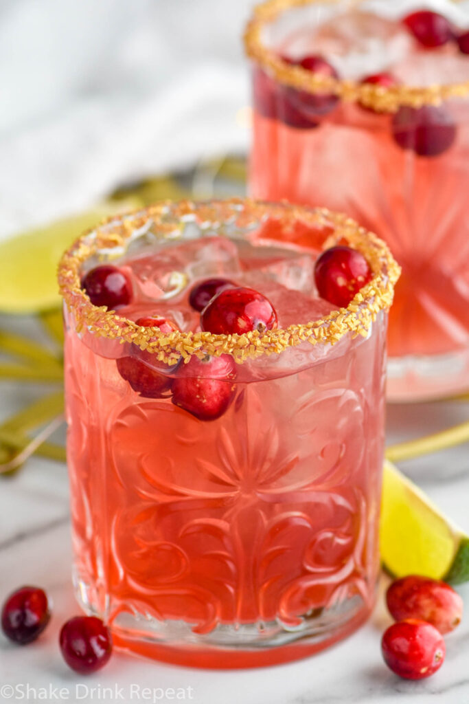 Overhead photo of a glass of cranberry margarita with a golden sugar rim and cranberries floating in the drink and around the glass and a lime wedge