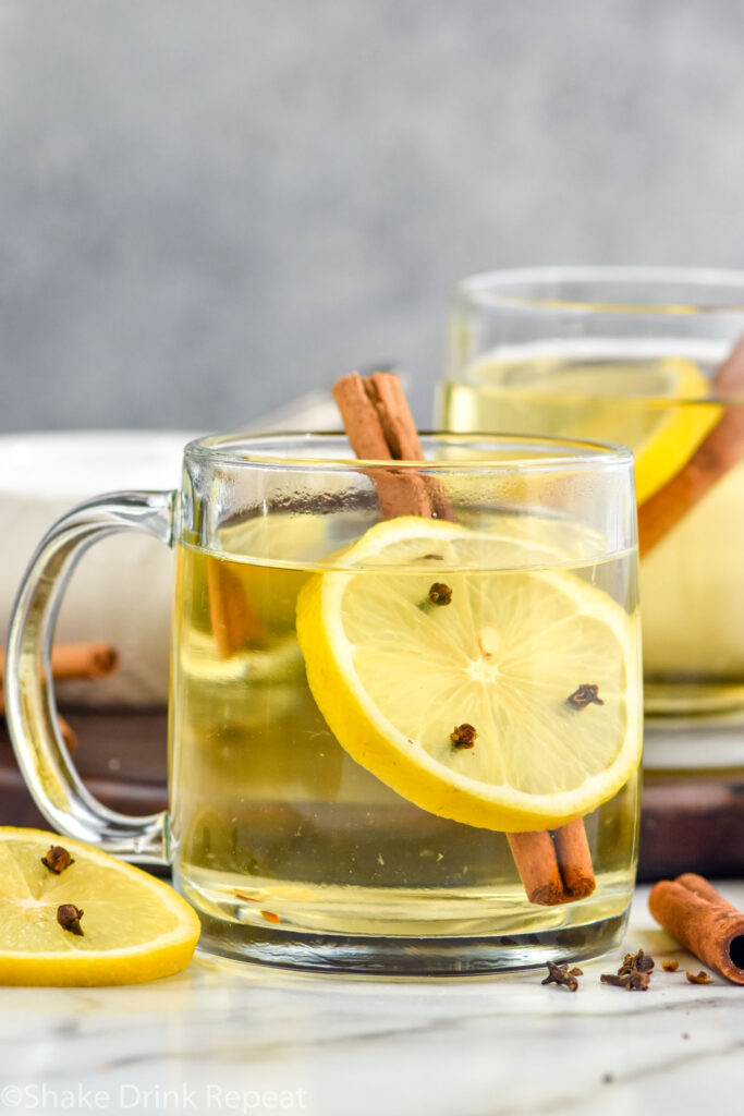 two mugs of hot toddy cocktail with a lemon slice with cloves and a cinnamon stick