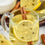 two mugs of hot toddy cocktail with a lemon slice with cloves and a cinnamon stick