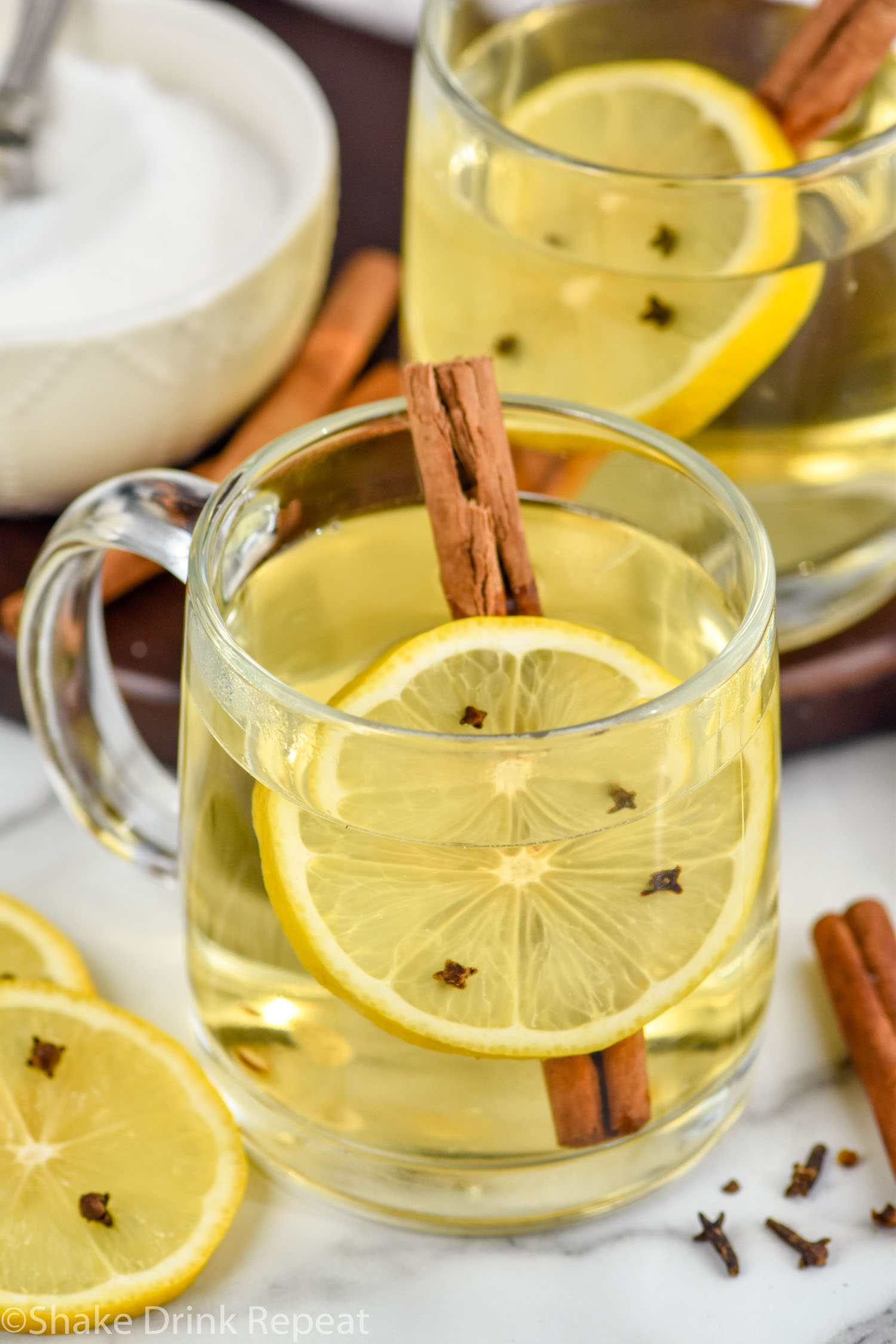 two mugs of hot toddy cocktail with a lemon slice with cloves and a cinnamon stick