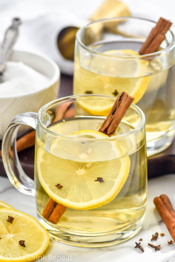 two mugs of hot toddy cocktail with a lemon slice with cloves and a cinnamon stick