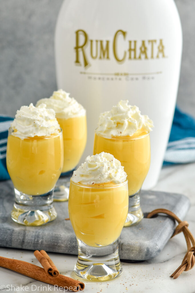 Overhead photo of RumChata Pudding Shots garnished with whipped cream. Bottle of RumChata in the background.