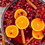 Overhead photo of Friendsmas Punch in a punch bowl with cinnamon sticks, orange slices, pomegranate seeds, and cranberries floating in the bowl and around the bowl.