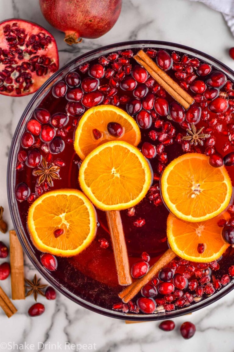 Overhead photo of Friendsmas Punch in a punch bowl with cinnamon sticks, orange slices, pomegranate seeds, and cranberries floating in the bowl and around the bowl.