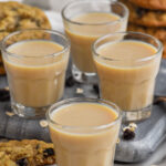 Front facing photo of four Oatmeal Cookie Shots with stacks of oatmeal cookies in the background.