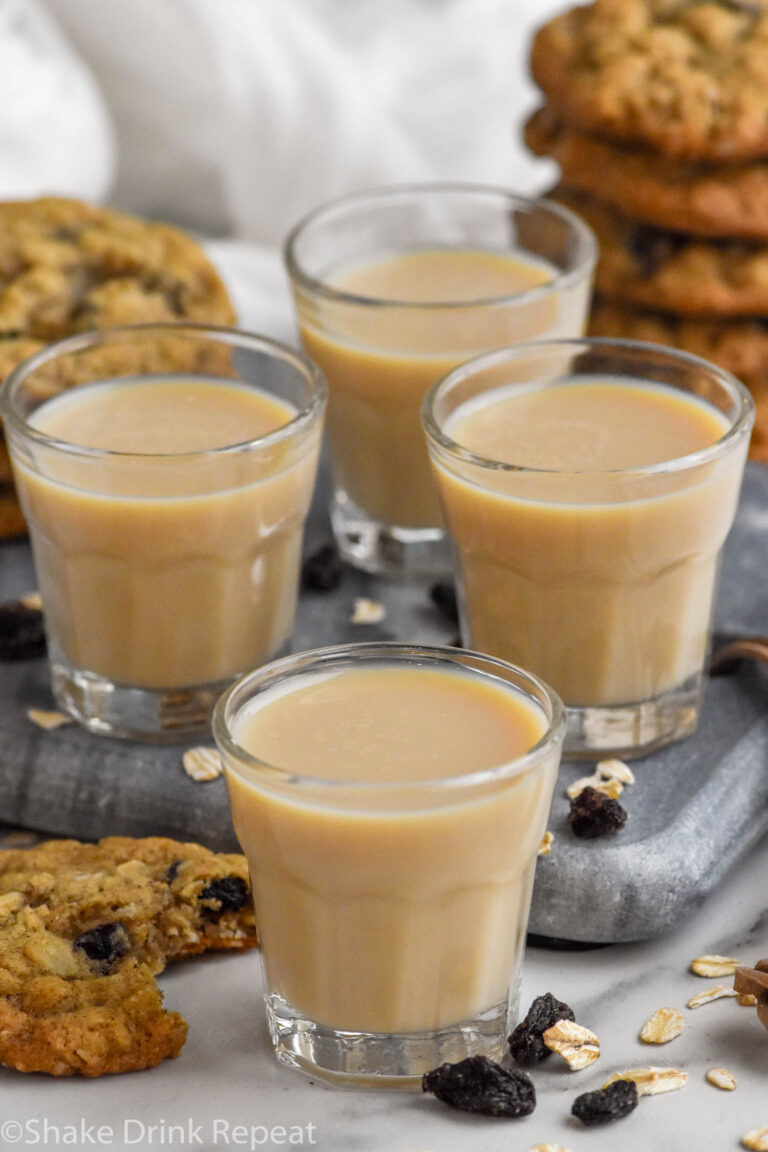 Front facing photo of four Oatmeal Cookie Shots with stacks of oatmeal cookies in the background.