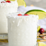 Pinterest photo of White Christmas Margarita with a front facing photo of the margarita in a clear cocktail glass with a lime and cranberry garnish. Says, 'White Christmas Margarita, shakedrinkrepeat.com'