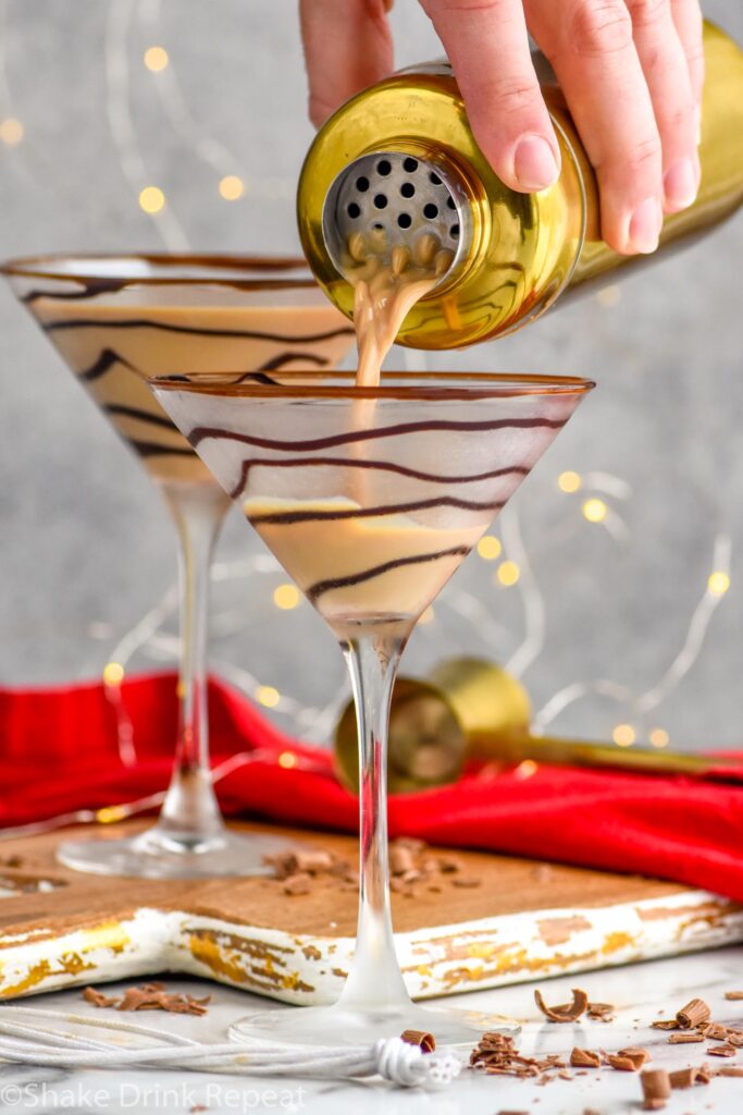 Front facing photo of Chocolate Martini being poured in a drizzled martini glass from a shaker with a prepared martini in the background.
