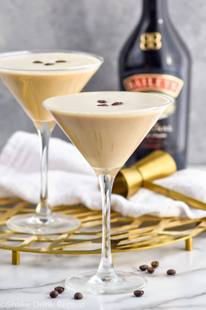 Close up photo of two Baileys Espresso Martini cocktails. Bottle of Baileys is behind cocktails.