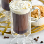 Overhead photo of mug of Irish Coffee topped with whipped cream. Bowl of brown sugar on counter behind mug.