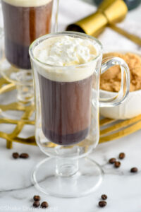 Overhead photo of mug of Irish Coffee topped with whipped cream. Bowl of brown sugar on counter behind mug.