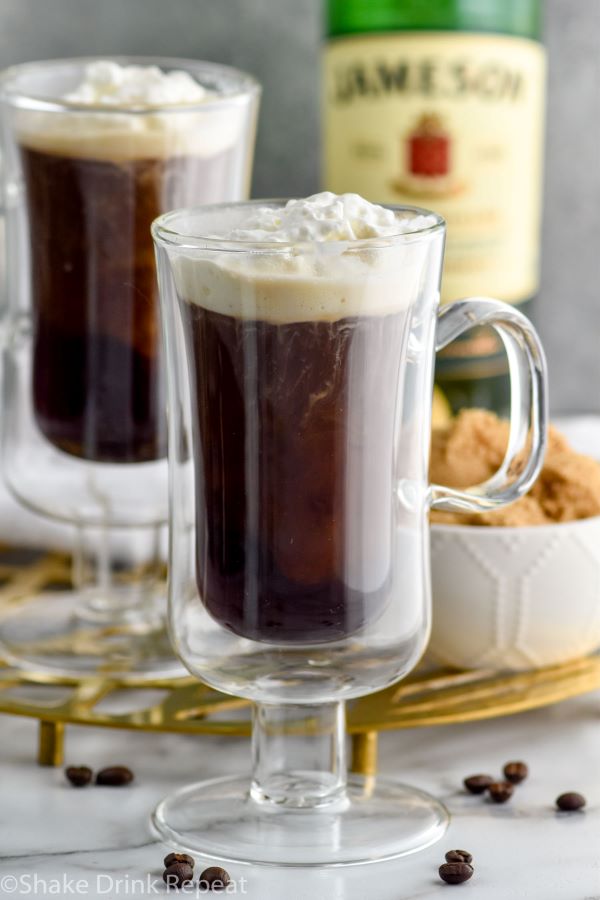 Close up photo of Irish Coffee. Brown sugar and bottle of Jameson in the background.