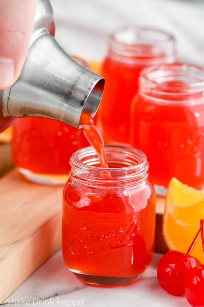 Photo of person's hand pouring shaker of Alabama Slammer Shot recipe into shot glass.