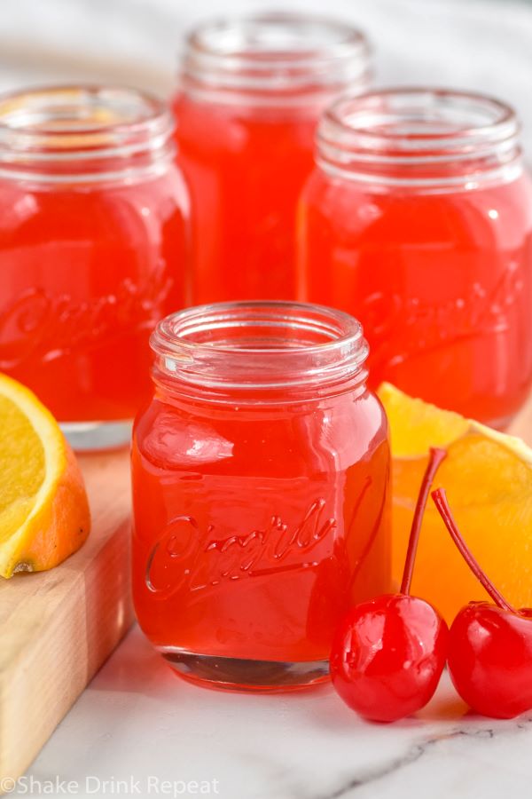 Close up photo of Alabama Slammer Shots. Orange slices and cherries sit beside shots.