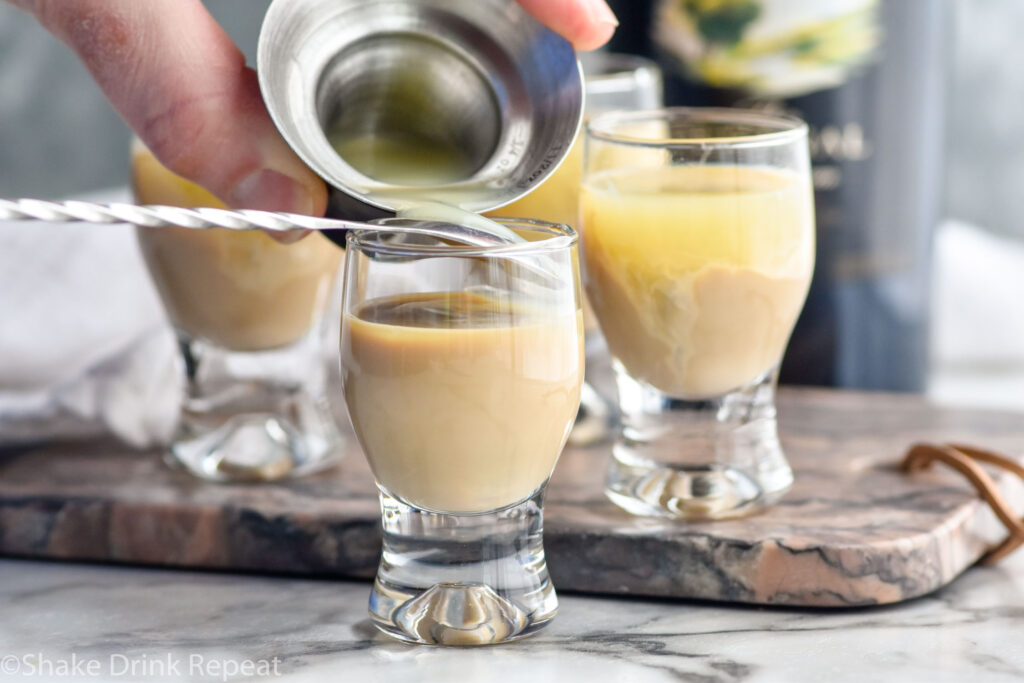 Photo of person's hands pouring lime juice over the back of a spoon into a shot glass of Irish cream liqueur for Cement Mixer Shot recipe