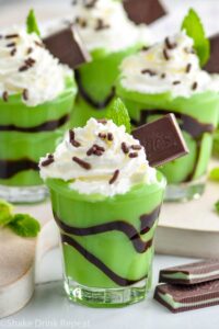 Close up photo of Grasshopper Pudding Shots garnished with whipped cream, mint leaf, and Andes Mint.
