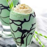 Close up photo of St. Patrick's Day mudslide garnished with whipped cream and sprinkles with straws for drinking.