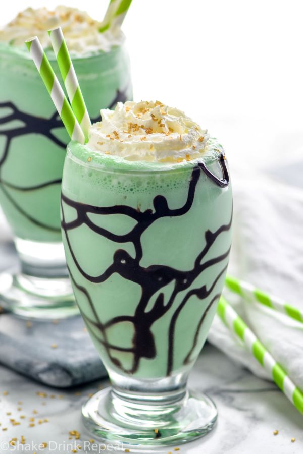 Close up photo of St. Patrick's Day mudslide garnished with whipped cream and sprinkles with straws for drinking.