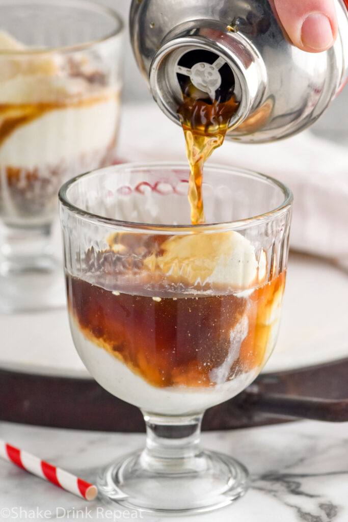 Photo of person's hand pouring a shaker bottle of ingredients into a glass of ice cream for White Russian Float recipe.