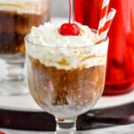 Photo of White Russian Float garnished with whipped cream and a cherry, with two straws for drinking.