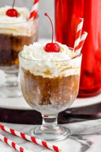 Photo of White Russian Float garnished with whipped cream and a cherry, with two straws for drinking.