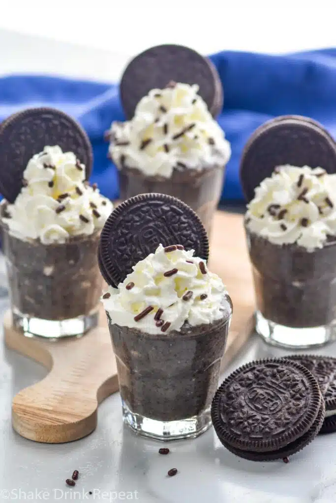 Overhead photo of Cookies and Cream Pudding Shots garnished with whipped cream, sprinkles, and Oreo cookies. Extra Oreo cookies on counter for garnish.