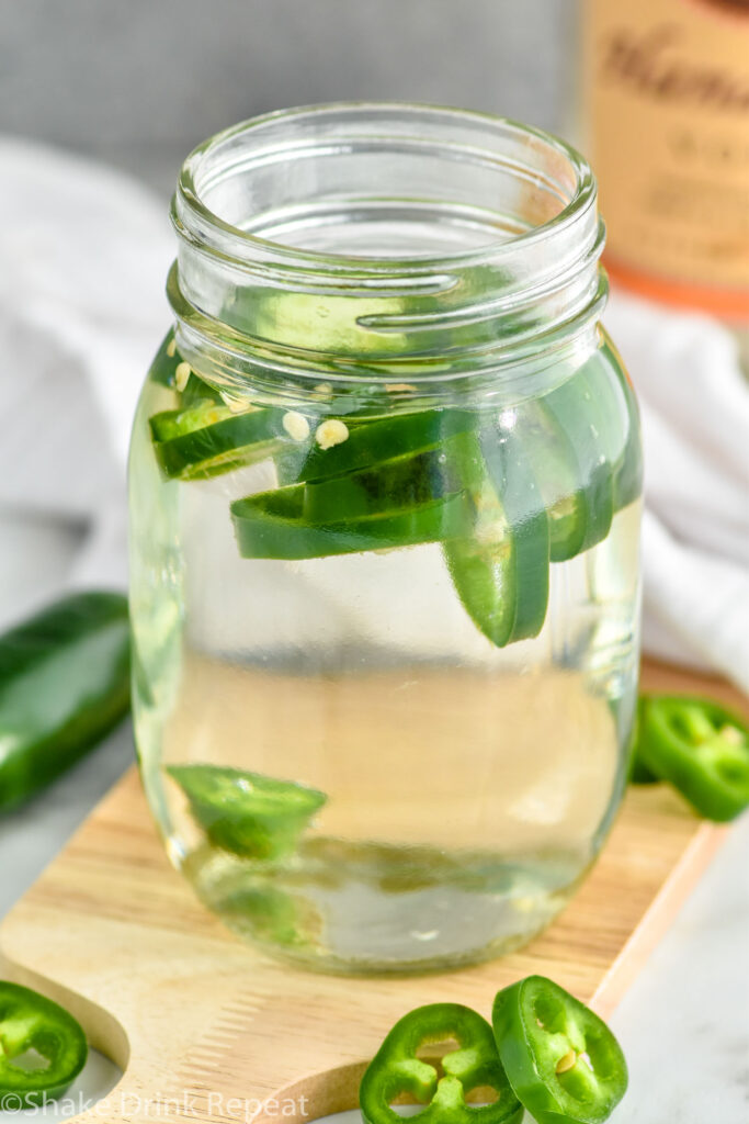 Close up photo of a jar of Jalapeno Infused Vodka recipe. Extra sliced jalapeno peppers beside jar.