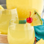 Photo of Pina Colada Sangria pitcher and two cocktails garnished with pineapple wedges and cherries.