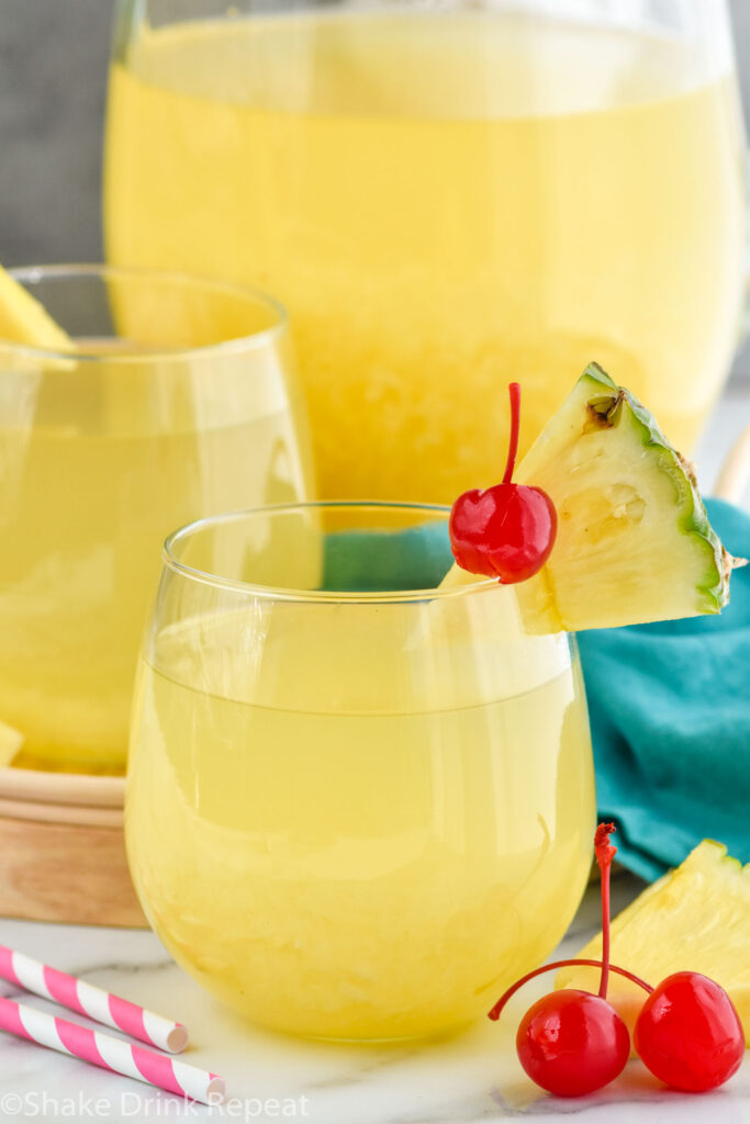 Photo of Pina Colada Sangria pitcher and two cocktails garnished with pineapple wedges and cherries.