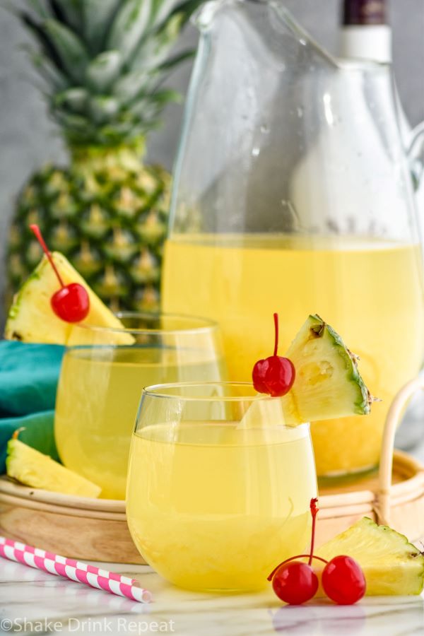 Photo of Pina Colada Sangria pitcher and two cocktails garnished with pineapple wedges and cherries.