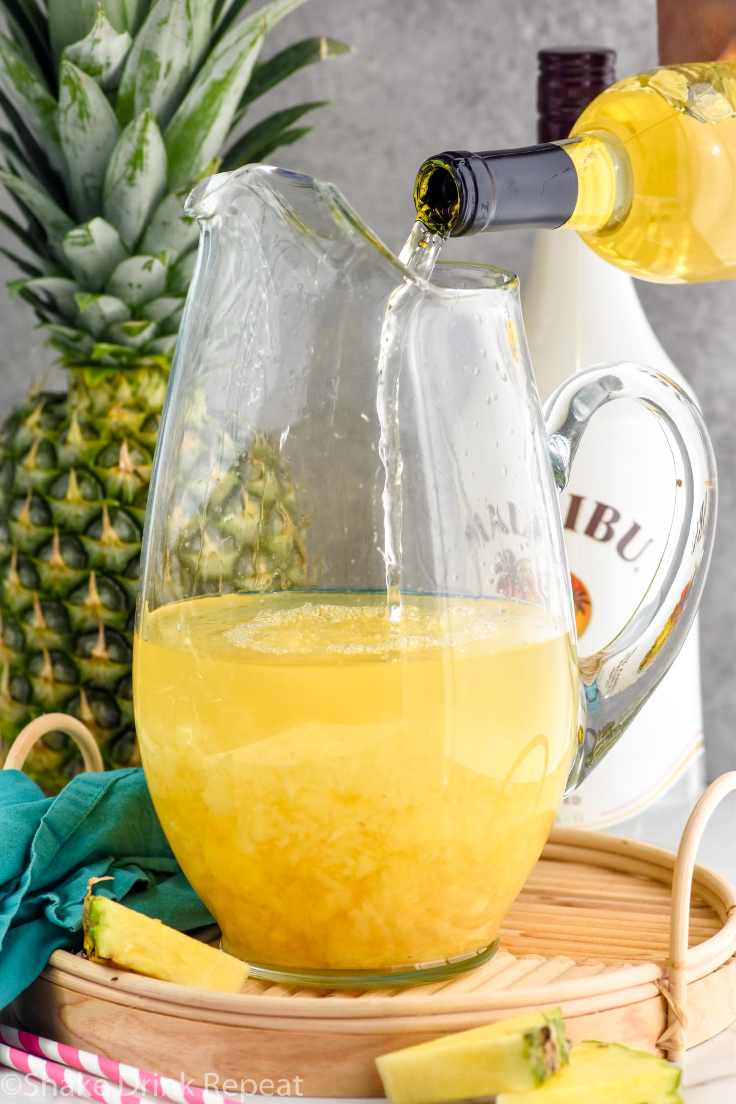 Photo of Moscato wine being poured into a pitcher of ingredients for Pina Colada Sangria recipe. Bottle of Malibu rum and a pineapple in the background.