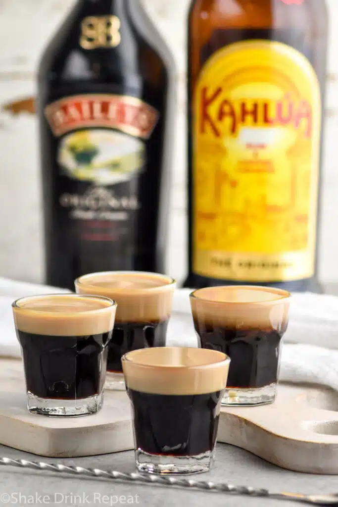 Side view of Baby Guinness Shots. Bottles of Bailey's and Kahlua in the background.