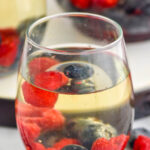 Side view of a glass of Fourth of July Sangria garnished with blueberries and strawberries. More glasses in the background.