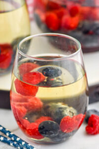 Side view of a glass of Fourth of July Sangria garnished with blueberries and strawberries. More glasses in the background.