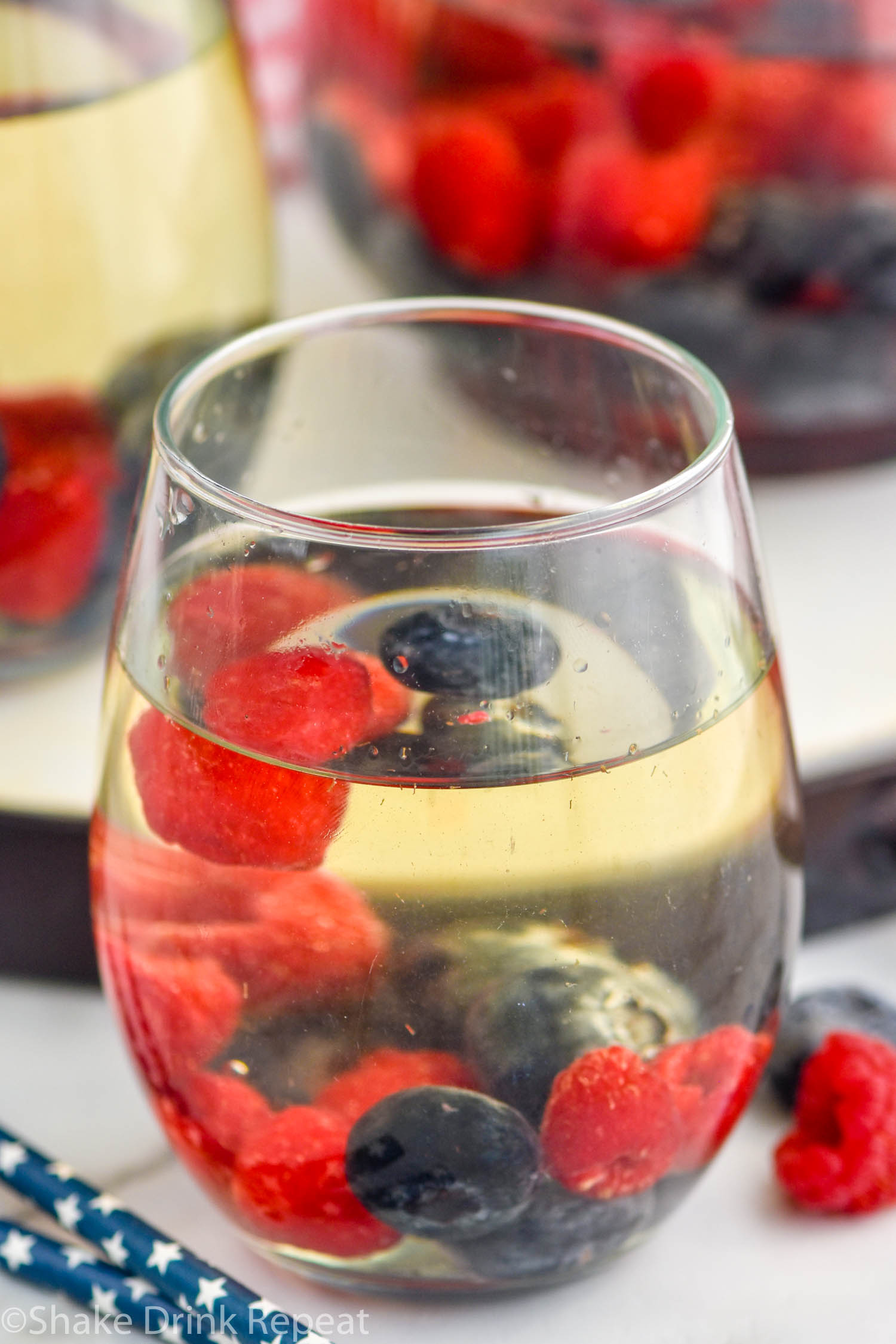 Side view of a glass of Fourth of July Sangria garnished with blueberries and strawberries. More glasses in the background.